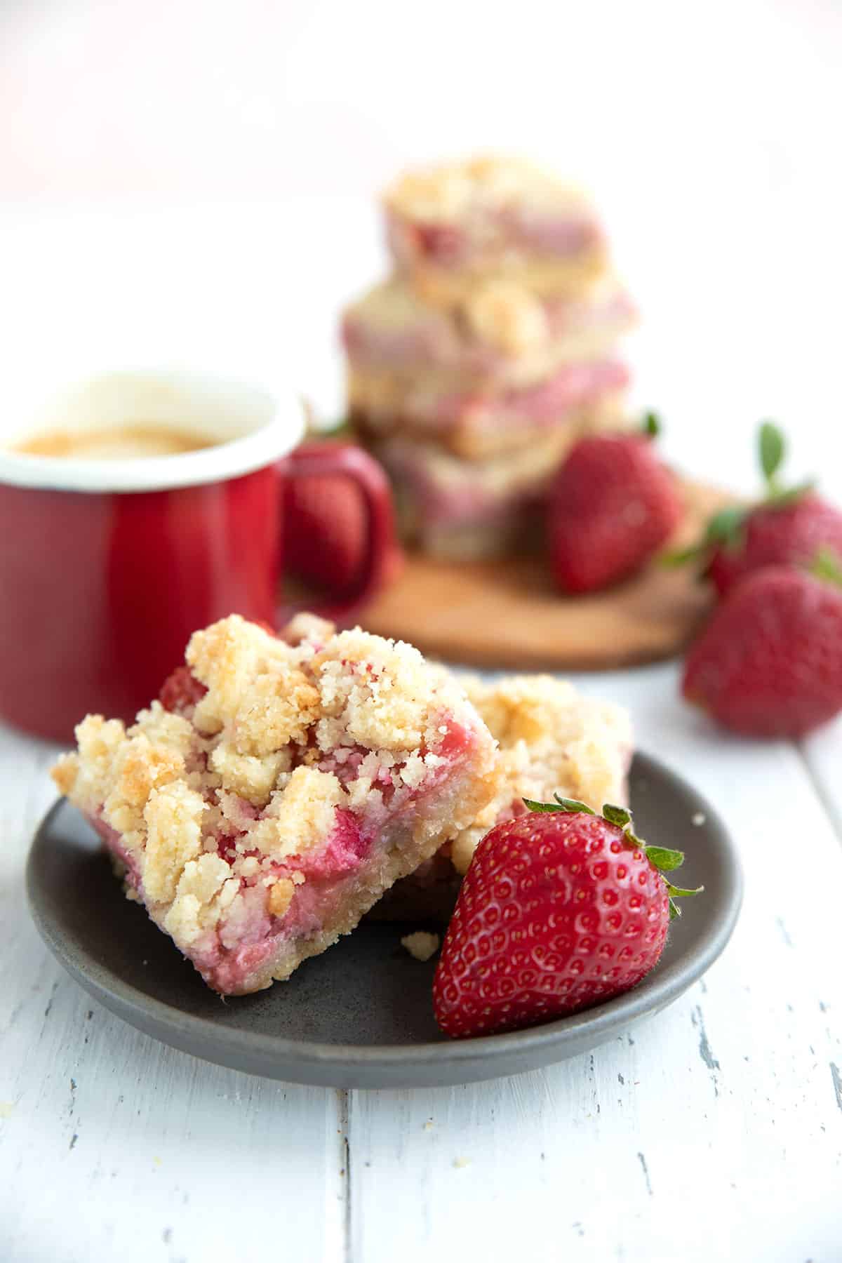 Two strawberry rhubarb crumb bars on a small gray plate with a strawberry.