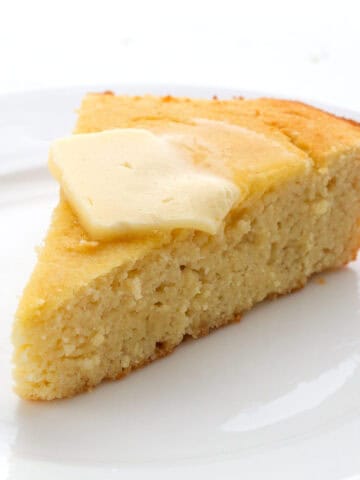 A slice of keto cornbread on a white plate with butter melting on top.