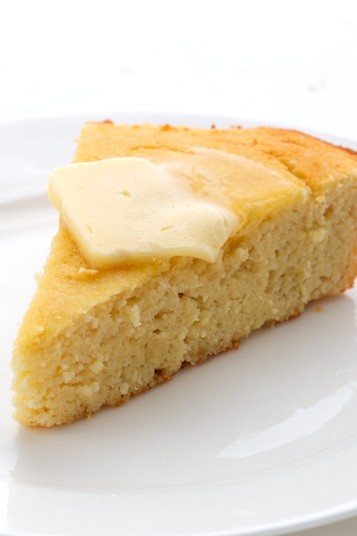 A slice of keto cornbread on a white plate with butter melting on top.