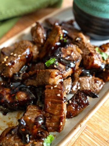 Asian Steak Bites piled up on a white platter with sesame seeds and cilantro.