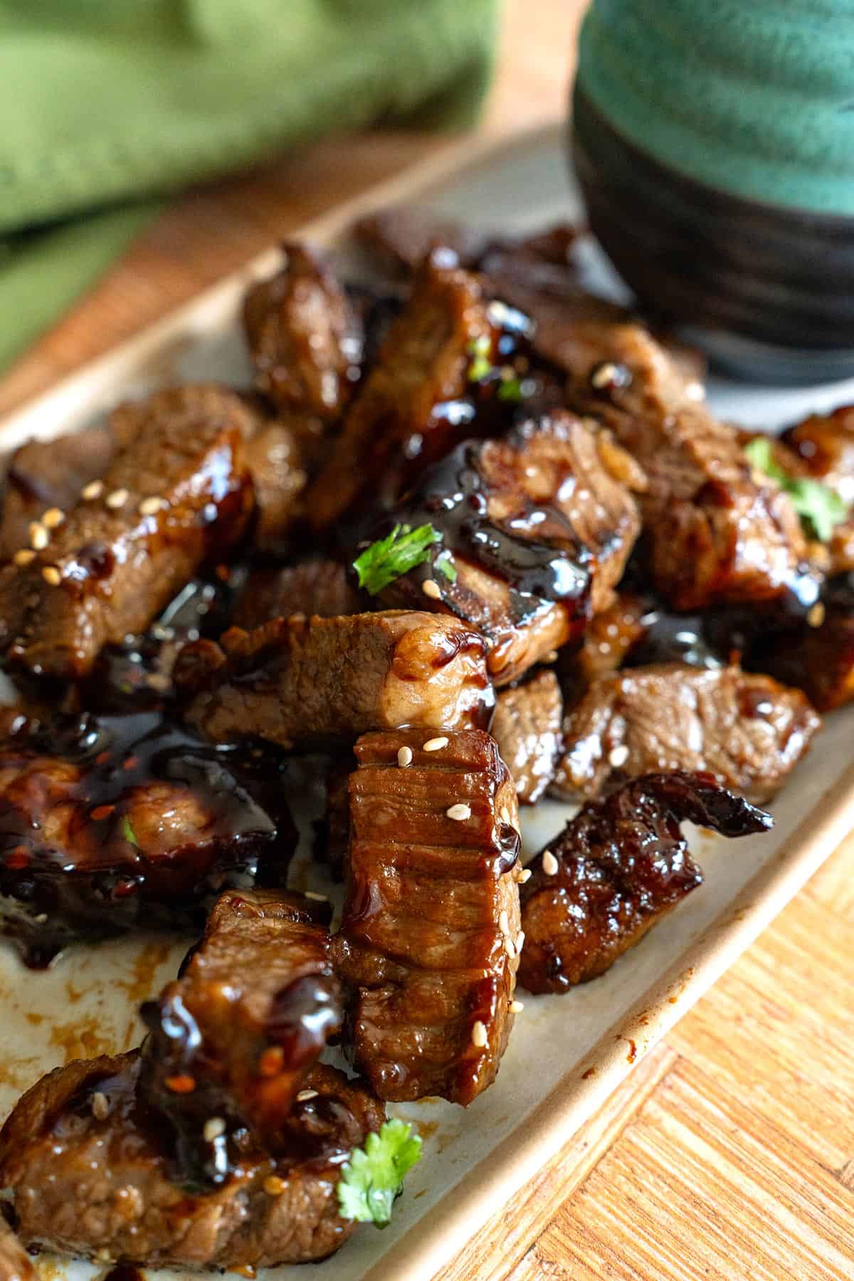 Asian Steak Bites piled up on a white platter with sesame seeds and cilantro.