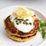 Close up shot of tuna patties on a white plate, topped with mayo, lemon, and capers.