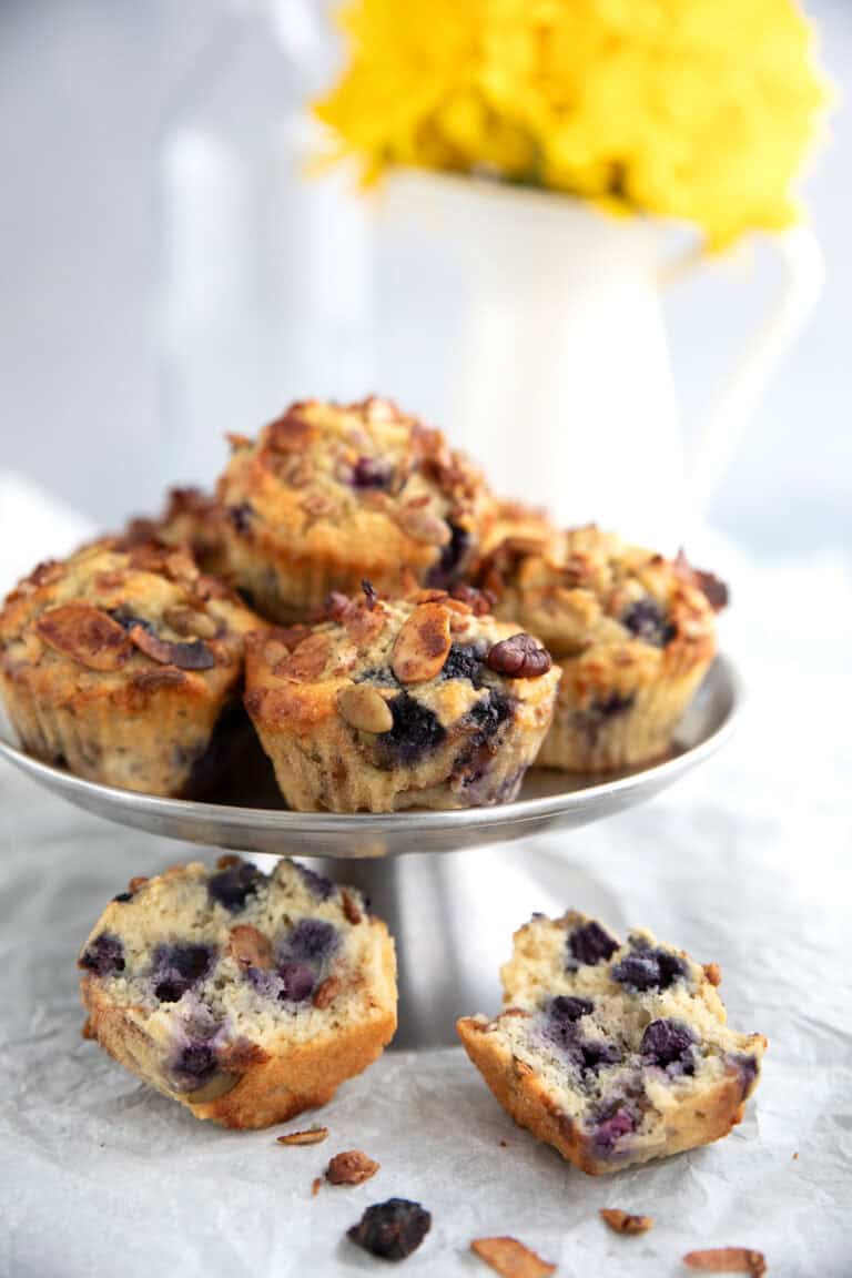 A stack of low carb granola muffins on a metal cake stand with one broken open in front.