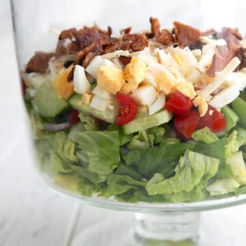 Keto 7 Layer Salad arranged in a trifle dish on a white wooden table.