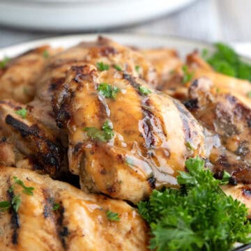 Close up shot of grilled Honey Mustard Chicken Thighs on a white plate with parsley.