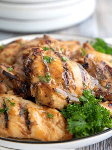 Close up shot of grilled Honey Mustard Chicken Thighs on a white plate with parsley.