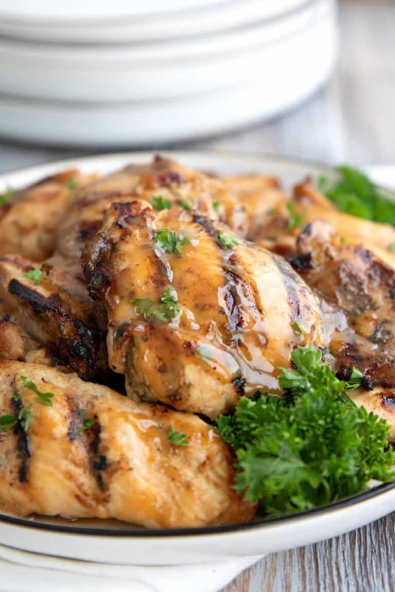 Close up shot of grilled Honey Mustard Chicken Thighs on a white plate with parsley.