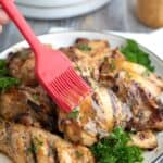 A red pastry brush brushing sugar free honey mustard glaze over grilled chicken thighs.