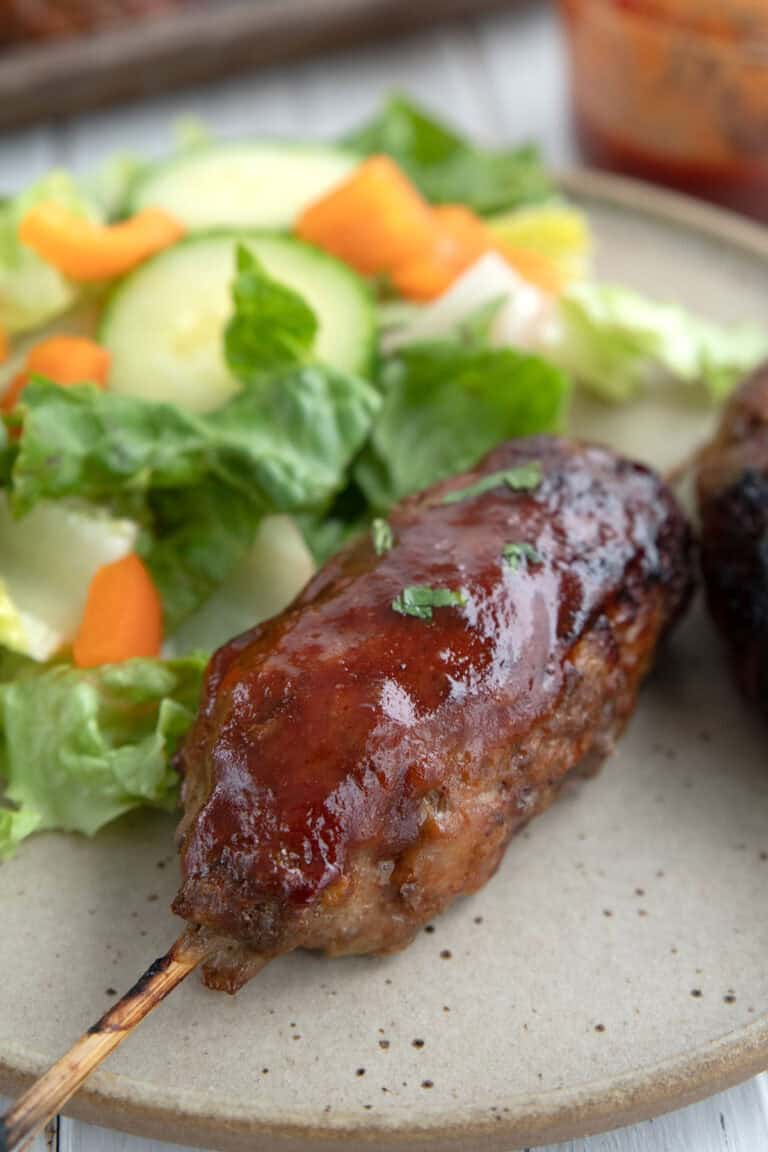 Close up shot of a BBQ Meatloaf Skewer on a plate with salad.