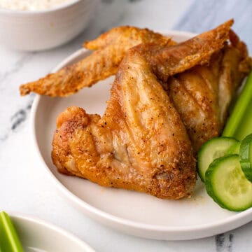 Two Old Bay Wings on a white plate with celery and cucumber.