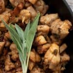 Titled image of brown butter chicken in a cast iron skillet with a sprig of fresh sage.