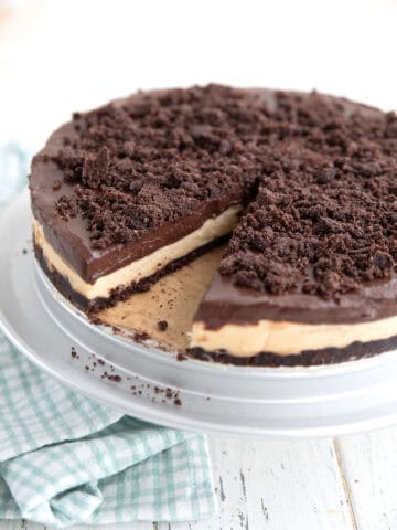 Keto Peanut Butter Dirt Cake with a slice taken out of it on a cake stand over a white table.