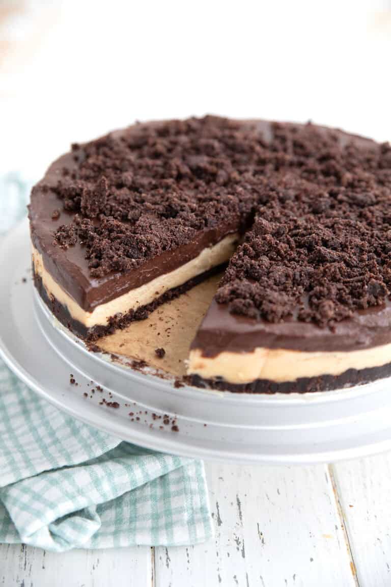 Keto Peanut Butter Dirt Cake with a slice taken out of it on a cake stand over a white table.