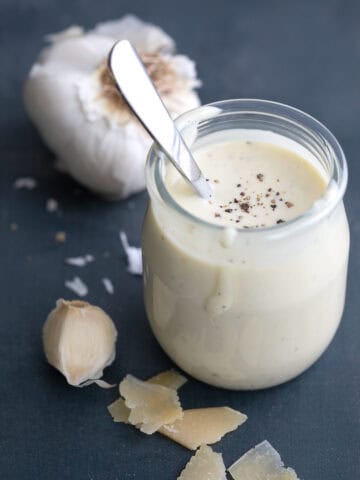 A jar of Easy Caesar Dressing surrounded by garlic and Parmesan.