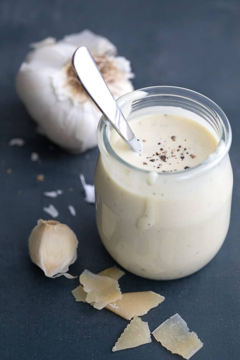 A jar of Easy Caesar Dressing surrounded by garlic and Parmesan.