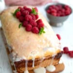 Keto Raspberry Swirl Bread topped with raspberries on a cutting board on a white table.