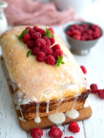 Keto Raspberry Swirl Bread topped with raspberries on a cutting board on a white table.