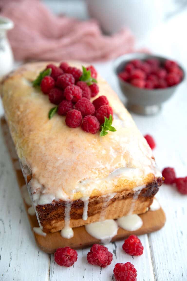 Keto Raspberry Swirl Bread topped with raspberries on a cutting board on a white table.