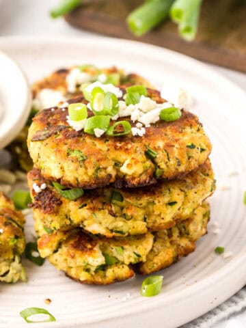 A stack of Keto Zucchini Fritters topped with green onion and feta.