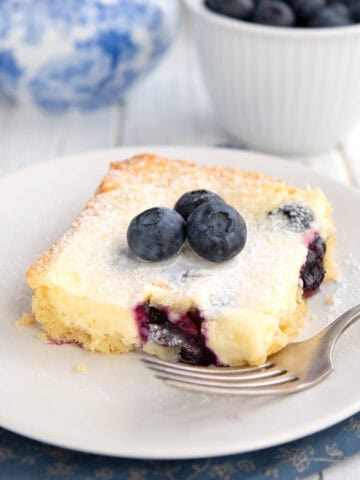 A slice of Keto Blueberry Lemon Gooey Butter Cake on a white plate with a fork.