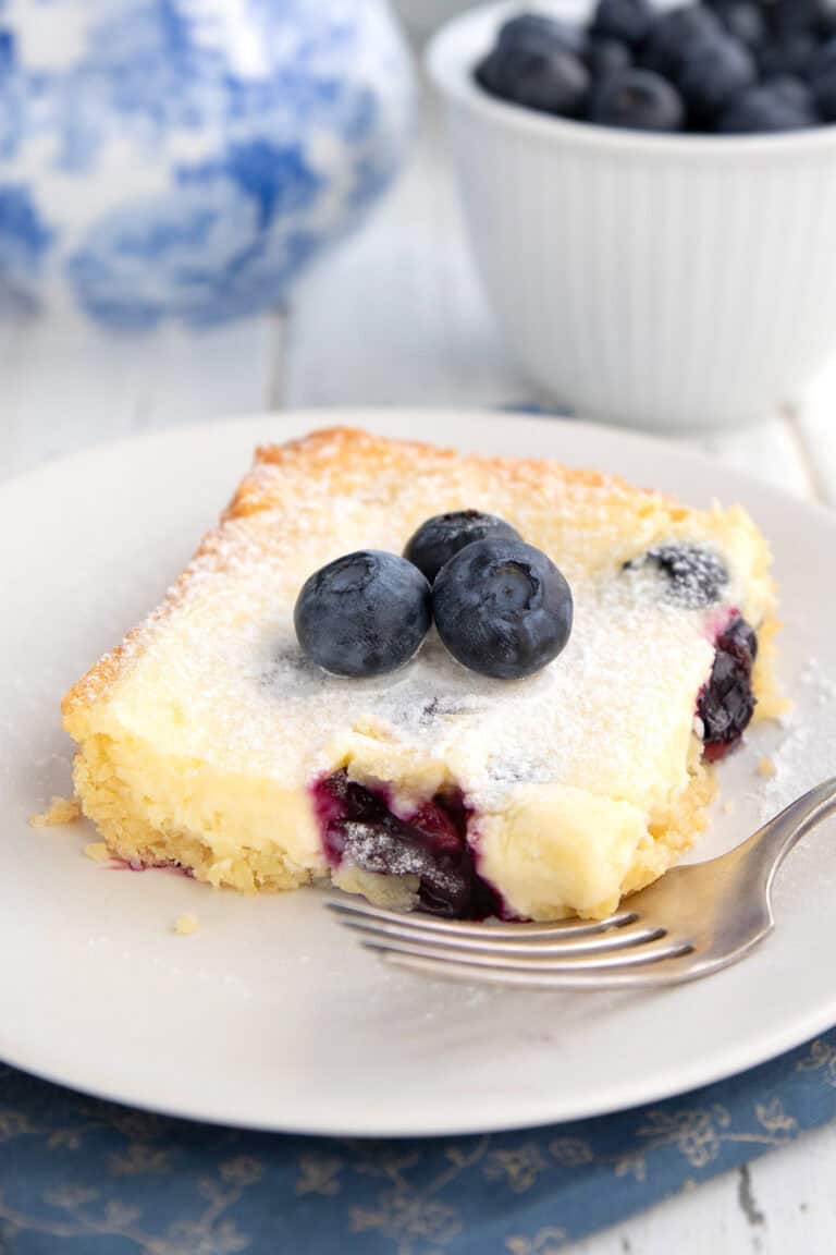 A slice of Keto Blueberry Lemon Gooey Butter Cake on a white plate with a fork.