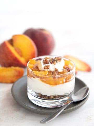 No Bake Keto Peach Cheesecake in a glass cup on a gray plate with peaches in the background.