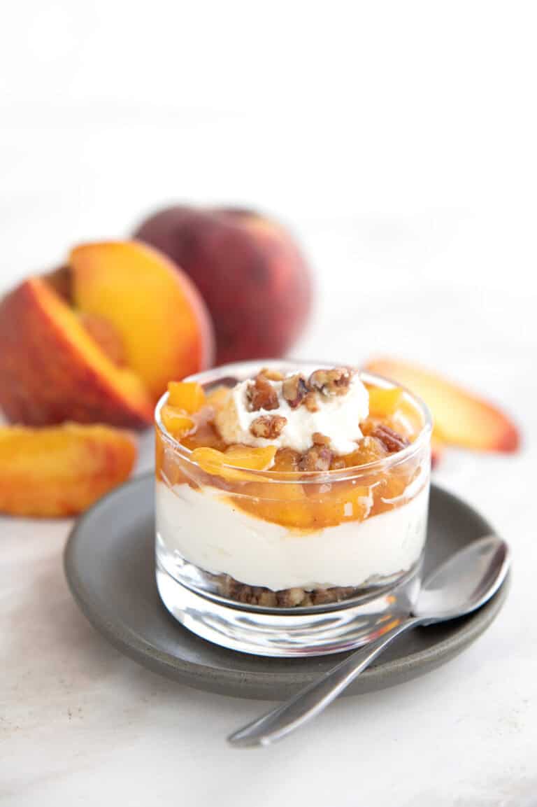 No Bake Keto Peach Cheesecake in a glass cup on a gray plate with peaches in the background.