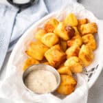 Air fryer pretzel bites in a white basket with a metal container filled with mustard dipping sauce.