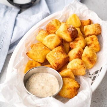 Air fryer pretzel bites in a white basket with a metal container filled with mustard dipping sauce.