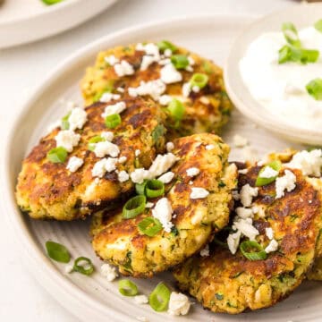 Keto Zucchini Fritters on a white plate, topped with feta and green onion.