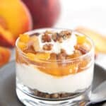 Easy Keto Peach Cheesecake in a glass dessert cup on a gray plate.