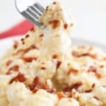 A fork holding up a pieces of cheesy slow cooker cauliflower.