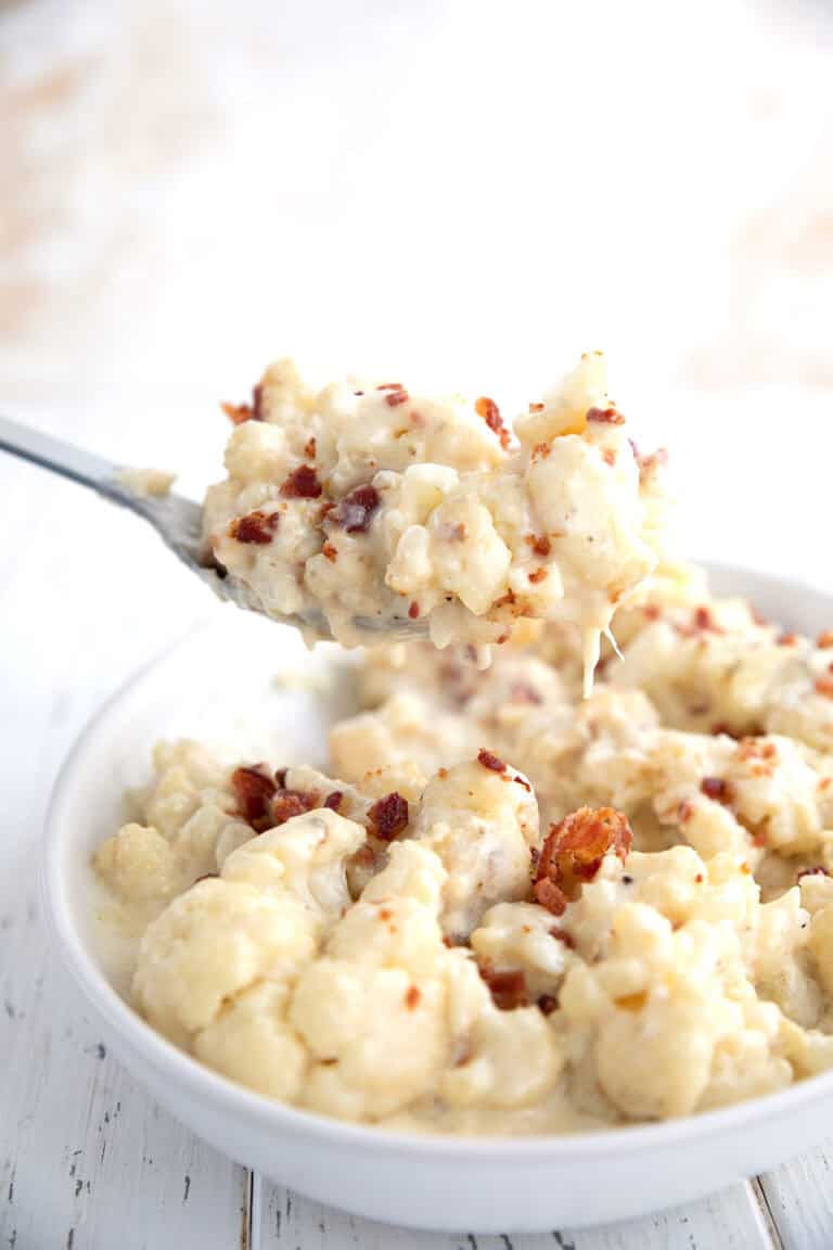 A serving spoon lifting slow cooker cauliflower out of a bowl.