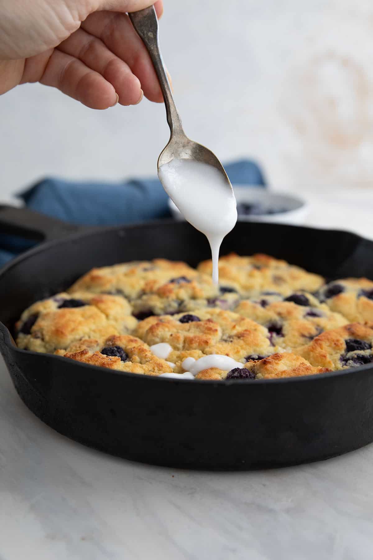 A spoon drizzling lemon glaze over a pan of Keto Blueberry Biscuits.