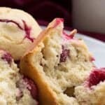 Titled image of keto cranberry muffins on a white plate, with one split open to show the inside.