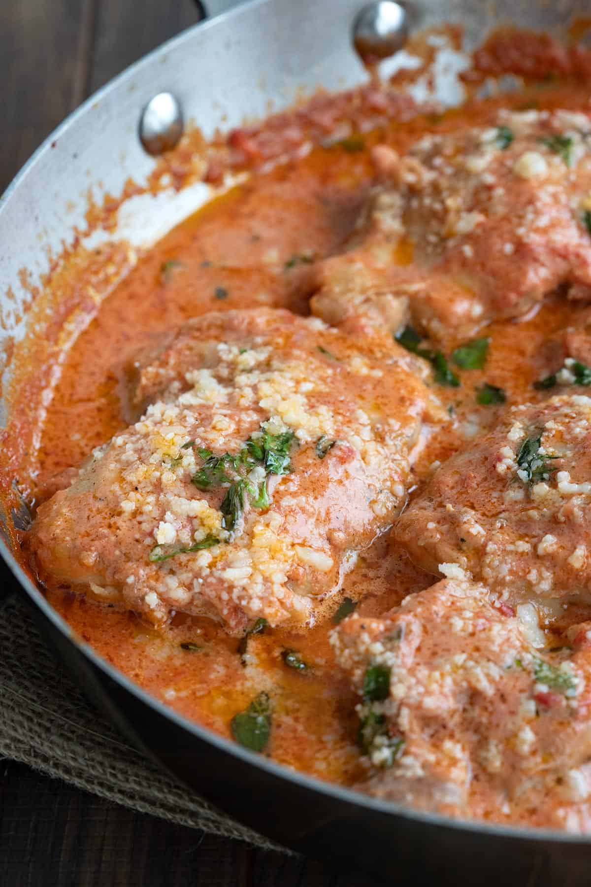 Close up shot of creamy tomato basil chicken in a stainless steel skillet.