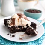 A slice of Keto Slow Cooker Chocolate Cake on a white plate over a teal napkin, with ice cream melting on top.