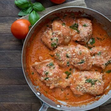 Top down image of Tomato Basil Chicken in a skillet on a brown wooden table.