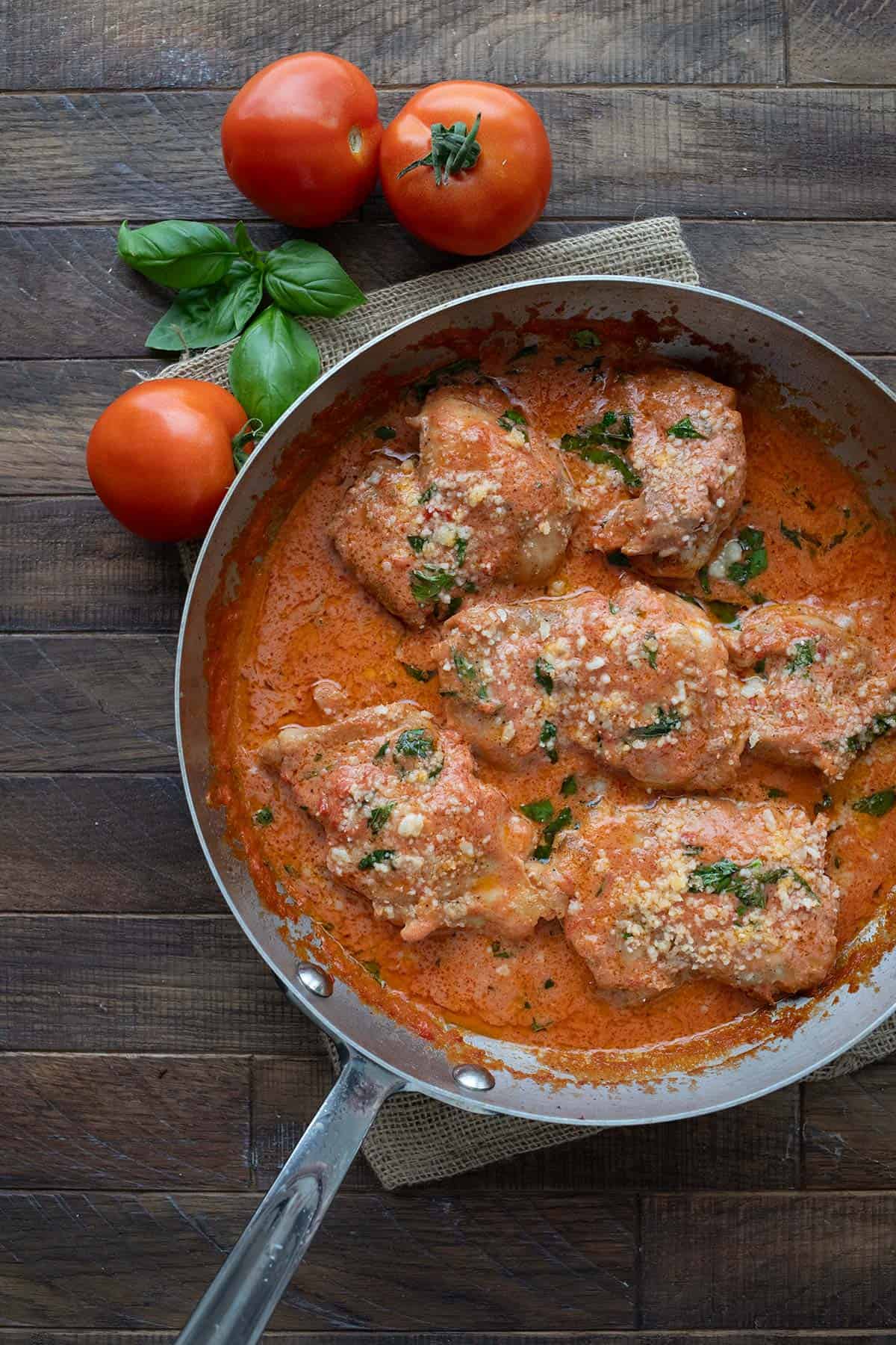 Top down image of Tomato Basil Chicken in a skillet on a brown wooden table.