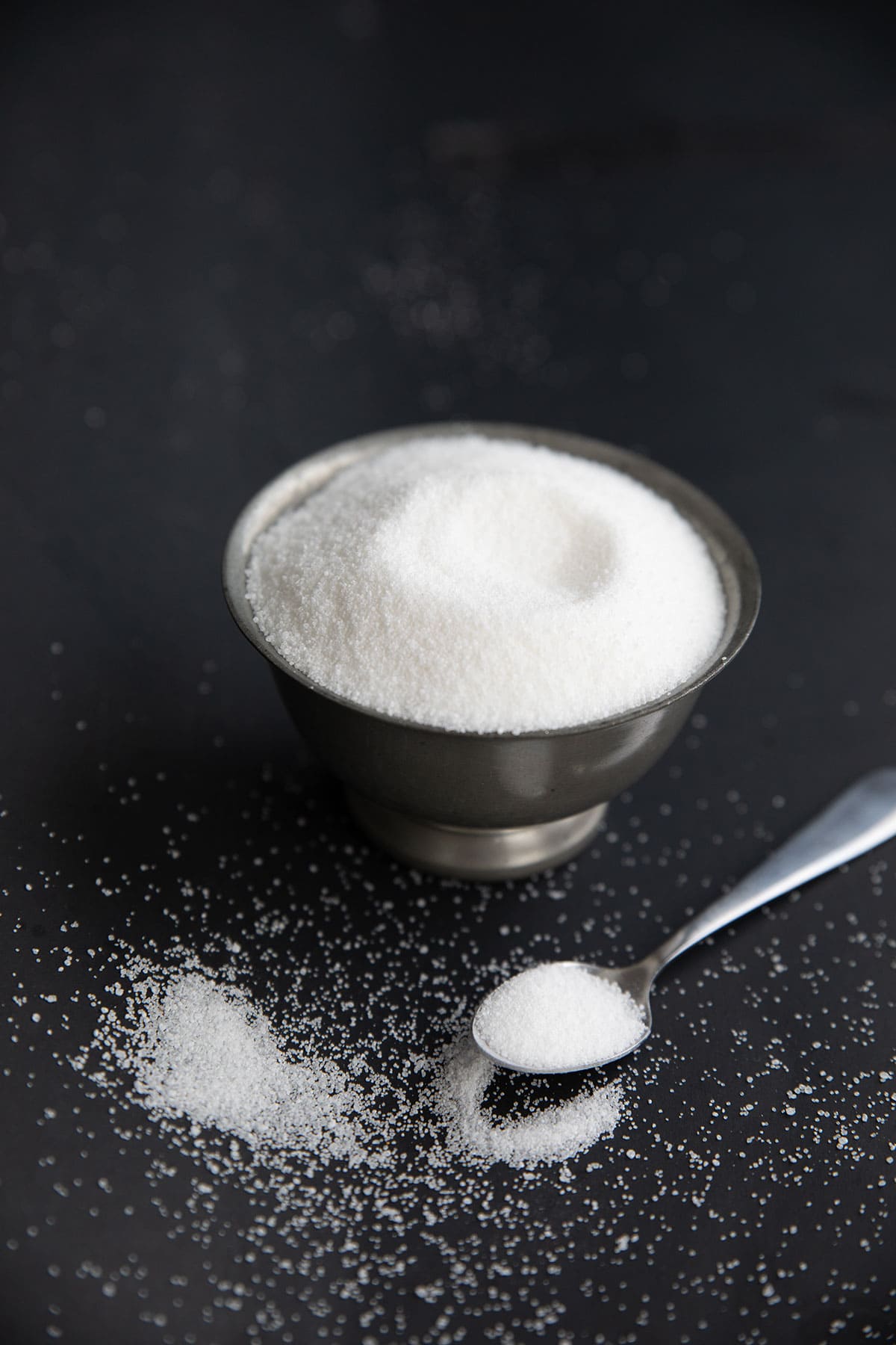 A metal bowl filled with erythritol sweetener on a black background.