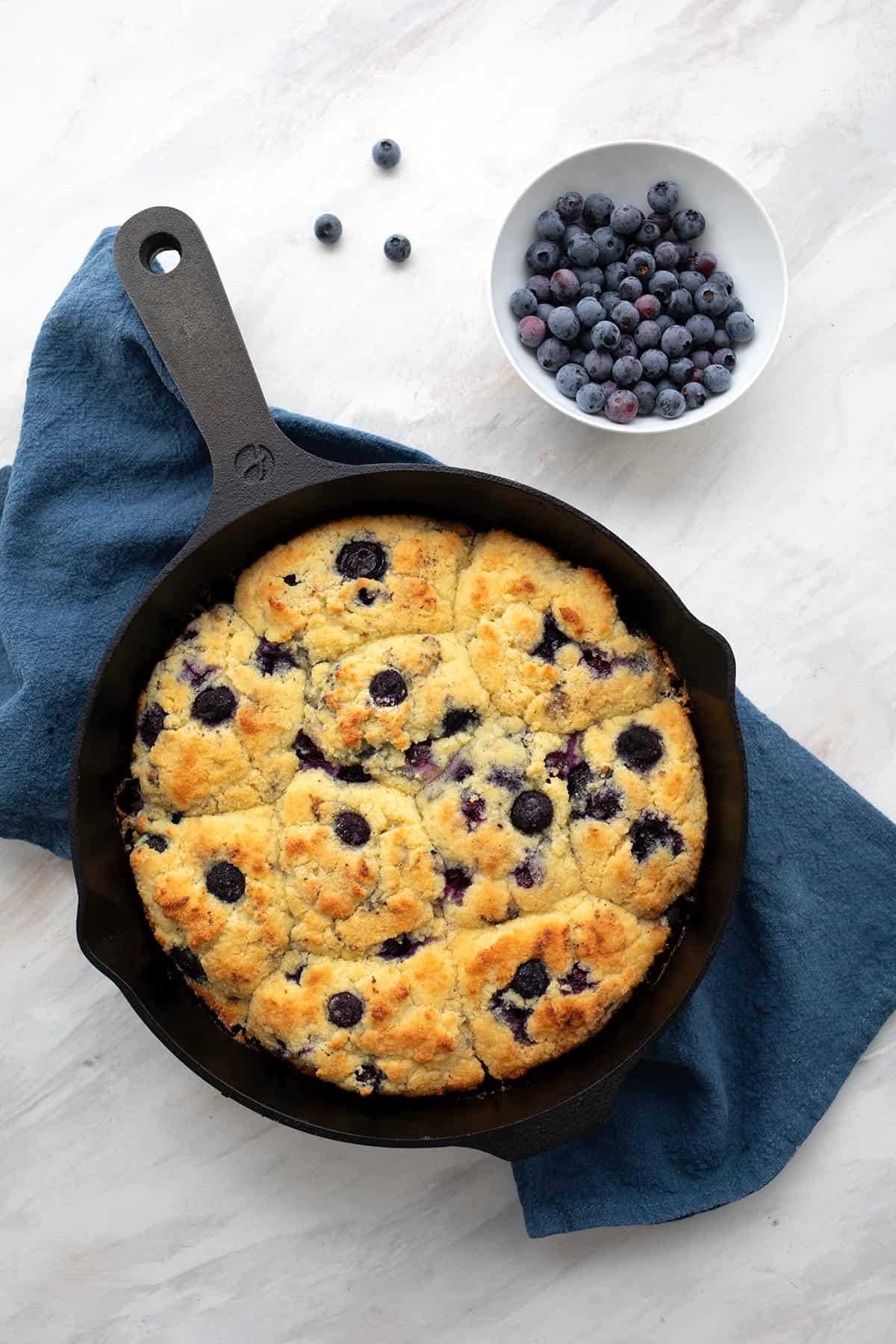 Top down image of a cast iron pan filled with freshly baked Keto Blueberry Biscuits over a blue napkin.