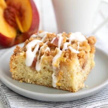 A slice of keto peach coffee cake on a gray plate with a white cup of coffee in the background.