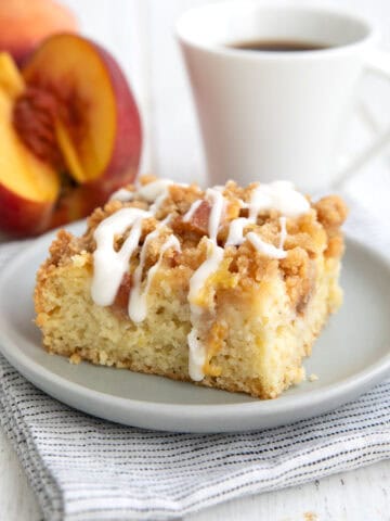 A slice of keto peach coffee cake on a gray plate with a white cup of coffee in the background.