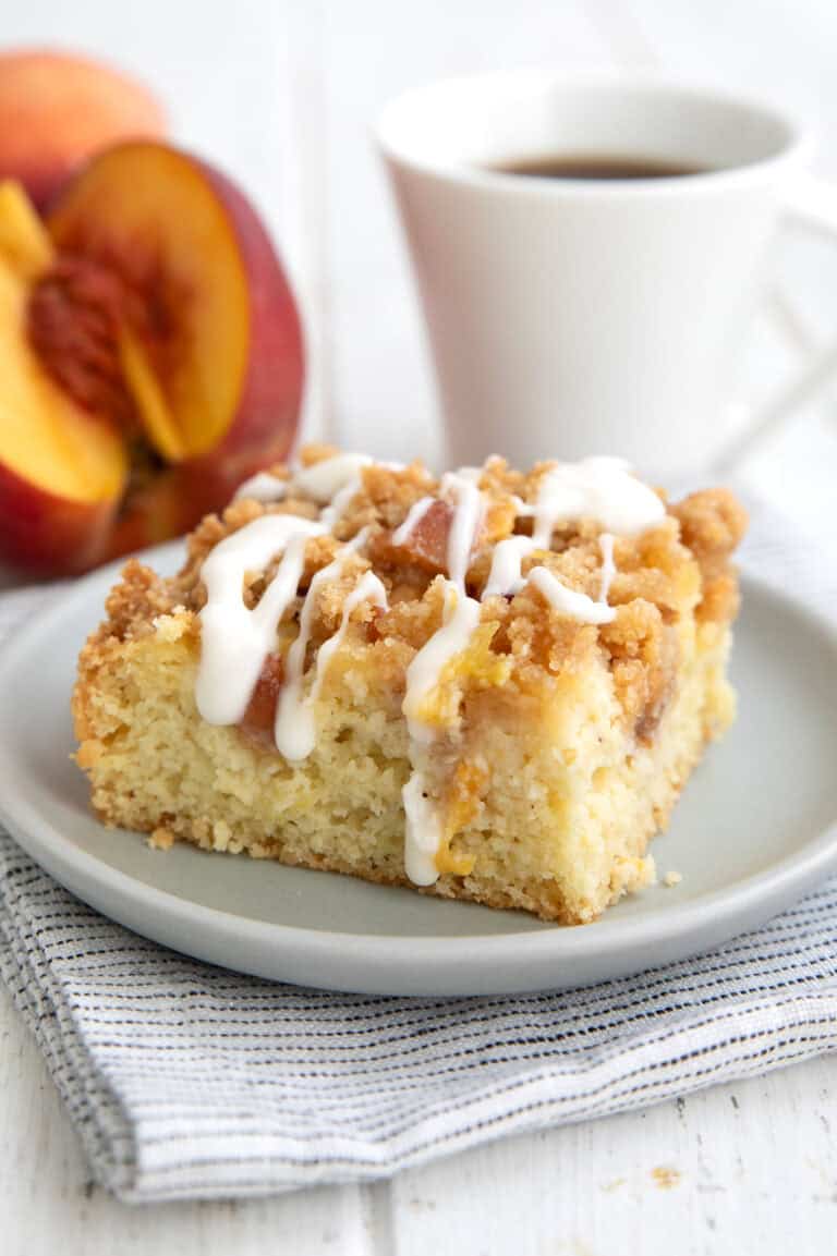 A slice of keto peach coffee cake on a gray plate with a white cup of coffee in the background.