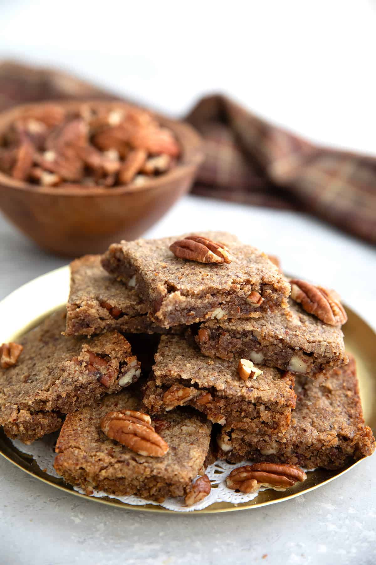 A pile of keto blondies on a metal copper plate in front of a bowl of pecans.