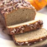 A loaf of Keto Pumpkin Bread with several slices in front, on a rustic wooden cutting board.