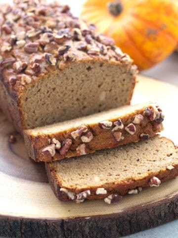 A loaf of Keto Pumpkin Bread with several slices in front, on a rustic wooden cutting board.