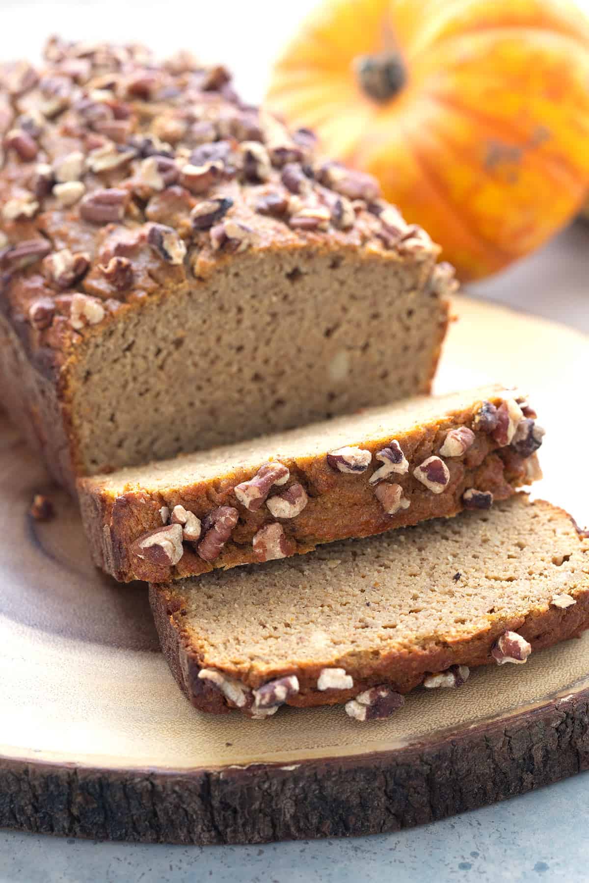 A loaf of Keto Pumpkin Bread with several slices in front, on a rustic wooden cutting board.