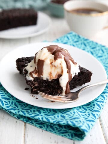 A slice of Keto Slow Cooker Chocolate Cake with ice cream and chocolate sauce on a white plate.