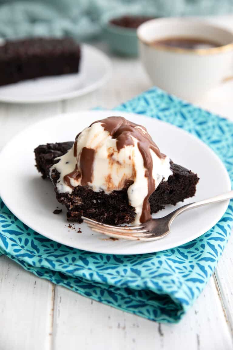 A slice of Keto Slow Cooker Chocolate Cake with ice cream and chocolate sauce on a white plate.